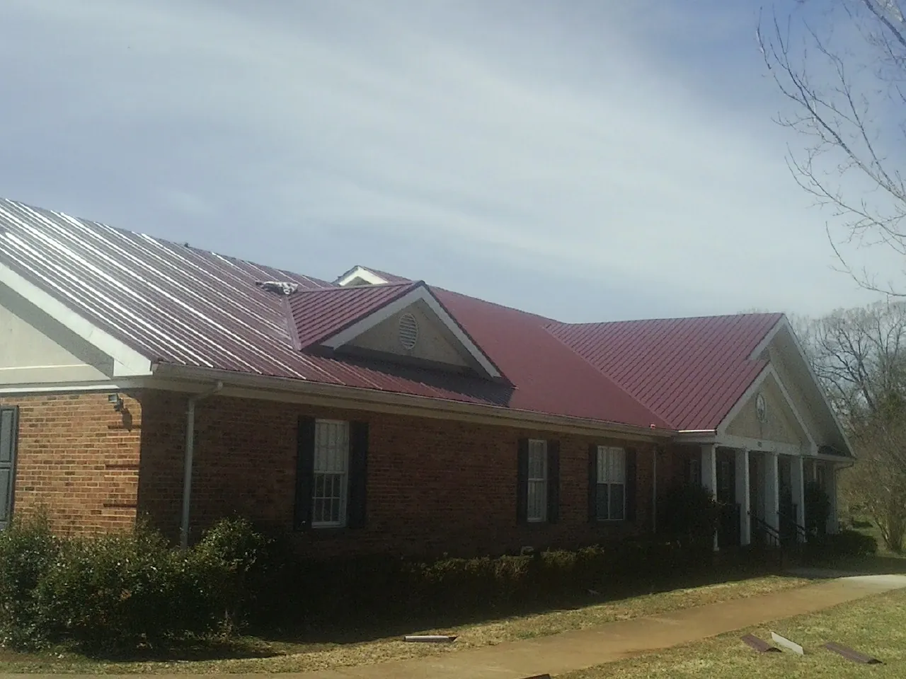 Red metal roof with gabled entries on a long brick building, from a Hail Damage Roof Repair job in Fort Jones