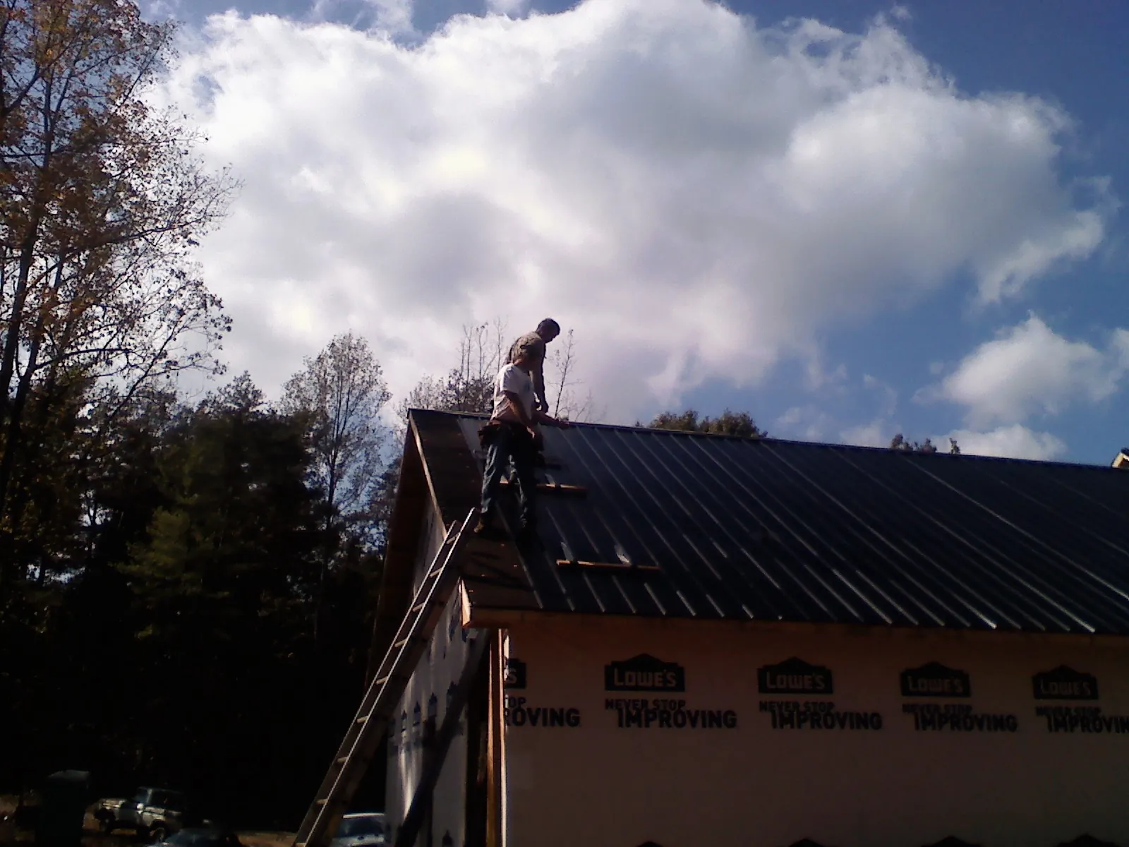 Roofer fastening dark metal panels high against a cloudy sky, from a Roof Inspection job in Fort Jones