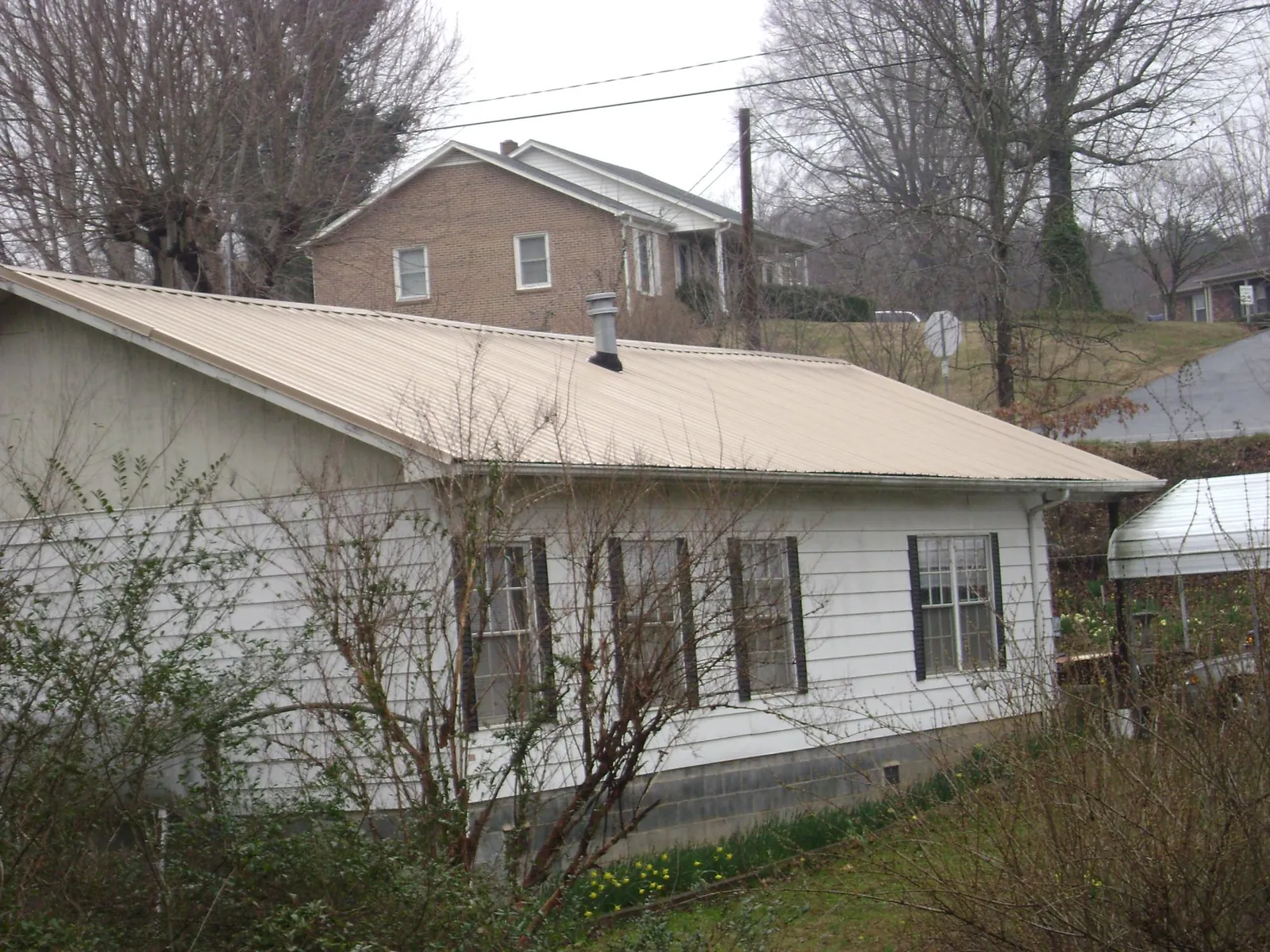 Tan metal roof on a white sided house set into a hillside — Commercial Roofing by Roofing Brothers in Fort Jones